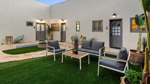 A modern outdoor patio with a white wall, grey door, and seating area with a coffee table and chairs. - Helios Boutique Suites by La Finca Hotel (Beersheba)