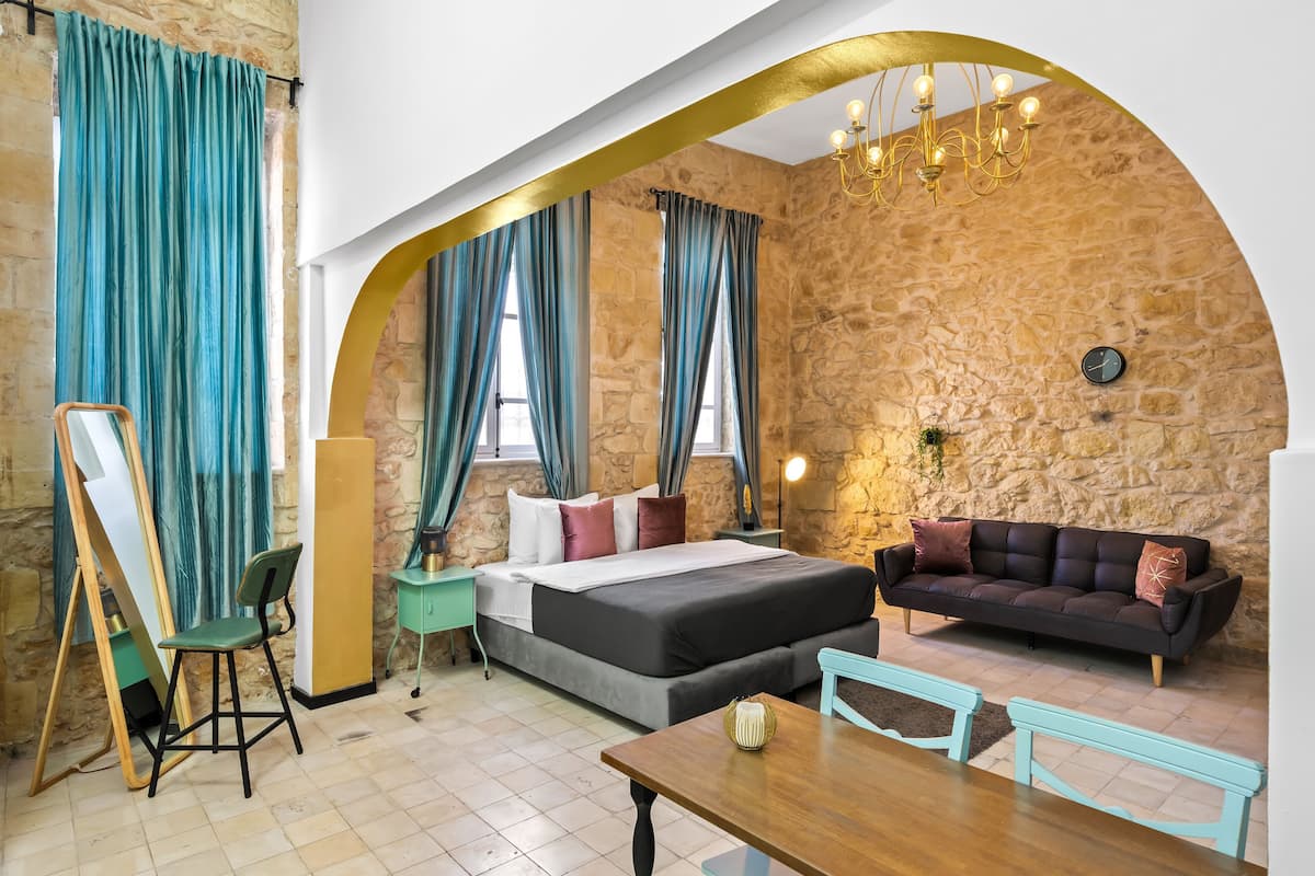 Ein Zimmer mit Steinwand, einem Bett, einer Couch, einem Esstisch und einem Stuhl.
