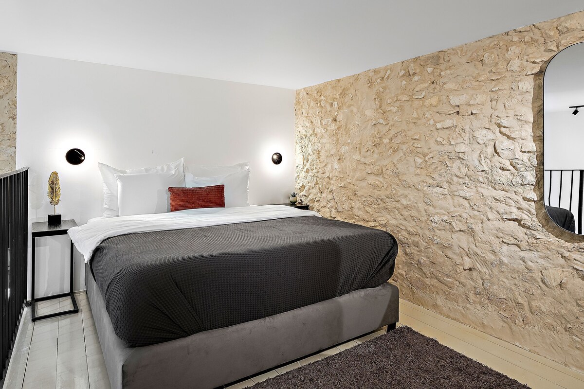 A bedroom with a bed, a nightstand, a wall-mounted mirror, and a textured wall.