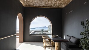 A modern interior with a dining area, a large arched window, and a view of the sea. - Serra Exclusive Suites (Santorini)