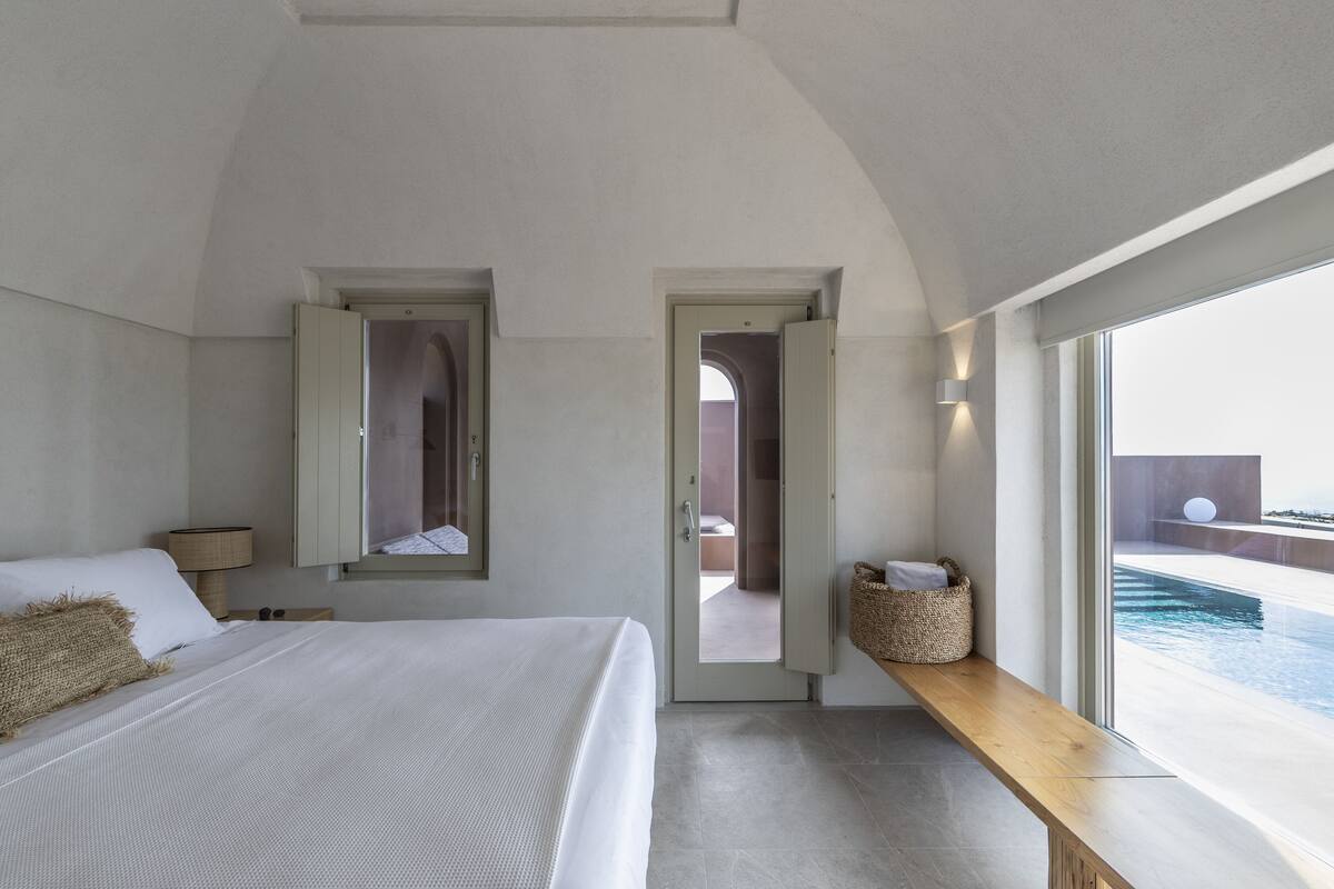 A modern bedroom with a large bed, a wooden bench, and a view of an infinity pool.