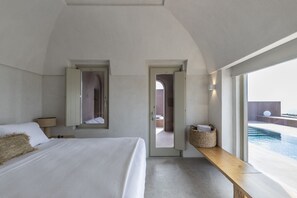 Un dormitorio moderno con una cama grande, un banco de madera y vistas a una piscina infinita.