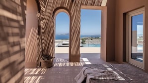 A modern room with a view of the sea, a bed, a window, and a small table with a basket. - Serra Exclusive Suites (Santorini)