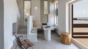 A modern interior with a seating area, a table with a bowl, a wooden stool, and a large window with a view. - Serra Exclusive Suites (Santorini)