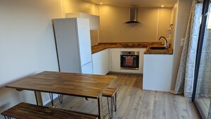 A compact kitchen with a wooden table and bench, a built-in oven, and a refrigerator.