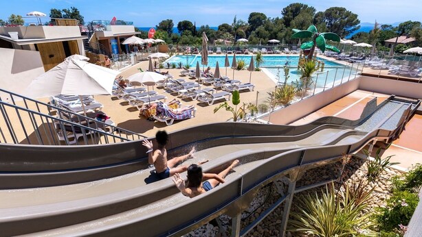 A water slide at a resort with a pool and lounge area.