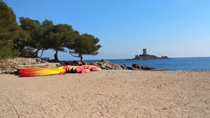 A beach with kayaks, trees, and a distant island with a tower.