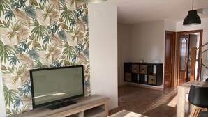 Una sala de estar con una televisión de pantalla plana sobre un mueble de madera, una mesa de centro y un papel tapiz estampado.