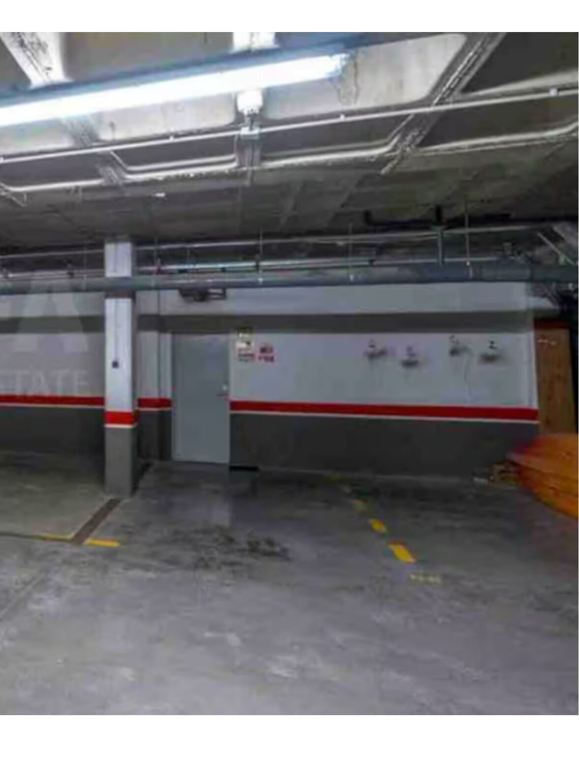 A parking garage with concrete pillars, a red and white stripe on the walls, and overhead fluorescent lighting.