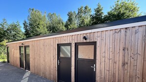 Ein Gebäude mit Holzfassade, zwei schwarzen Türen und einem gepflasterten Eingangsbereich.