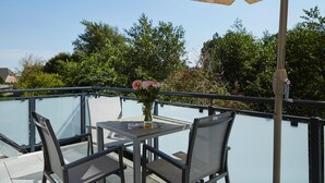 Ein Balkon mit Tisch, Stühlen, einer Blumenvase und einem großen Sonnenschirm.