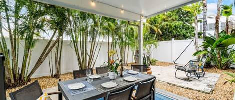 Une terrasse extérieure avec une table dressée pour le repas, entourée de chaises et d’un tapis bleu.