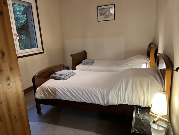 A bedroom with two wooden beds, white bedding, a framed picture on the wall, and a bedside lamp.