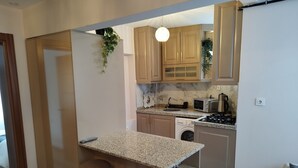 A compact kitchen with a granite countertop, wooden cabinets, a built-in oven, and a washing machine. - Cozy Home Next to Green Mosque (Bursa)