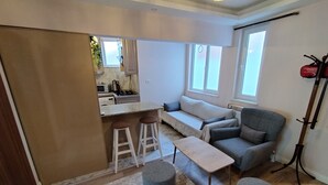 A compact living space with a kitchenette, a sofa, a coffee table, and two ottomans. - Cozy Home Next to Green Mosque (Bursa)