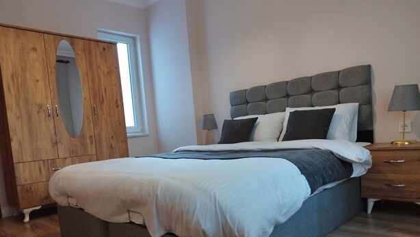 A bedroom with a large bed, wooden wardrobe, and a nightstand with a lamp. - Cozy Home Next to Green Mosque (Bursa)