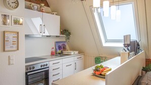 Une cuisine équipée d’un four encastré, d’un évier et d’une fenêtre offrant une vue agréable. On y trouve des placards, une horloge et un panneau d’accueil encadré.