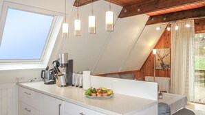 Une cuisine moderne avec un plan de travail blanc, une machine à café et un panier de fruits. Une fenêtre offre une vue sur la verdure à l'extérieur.