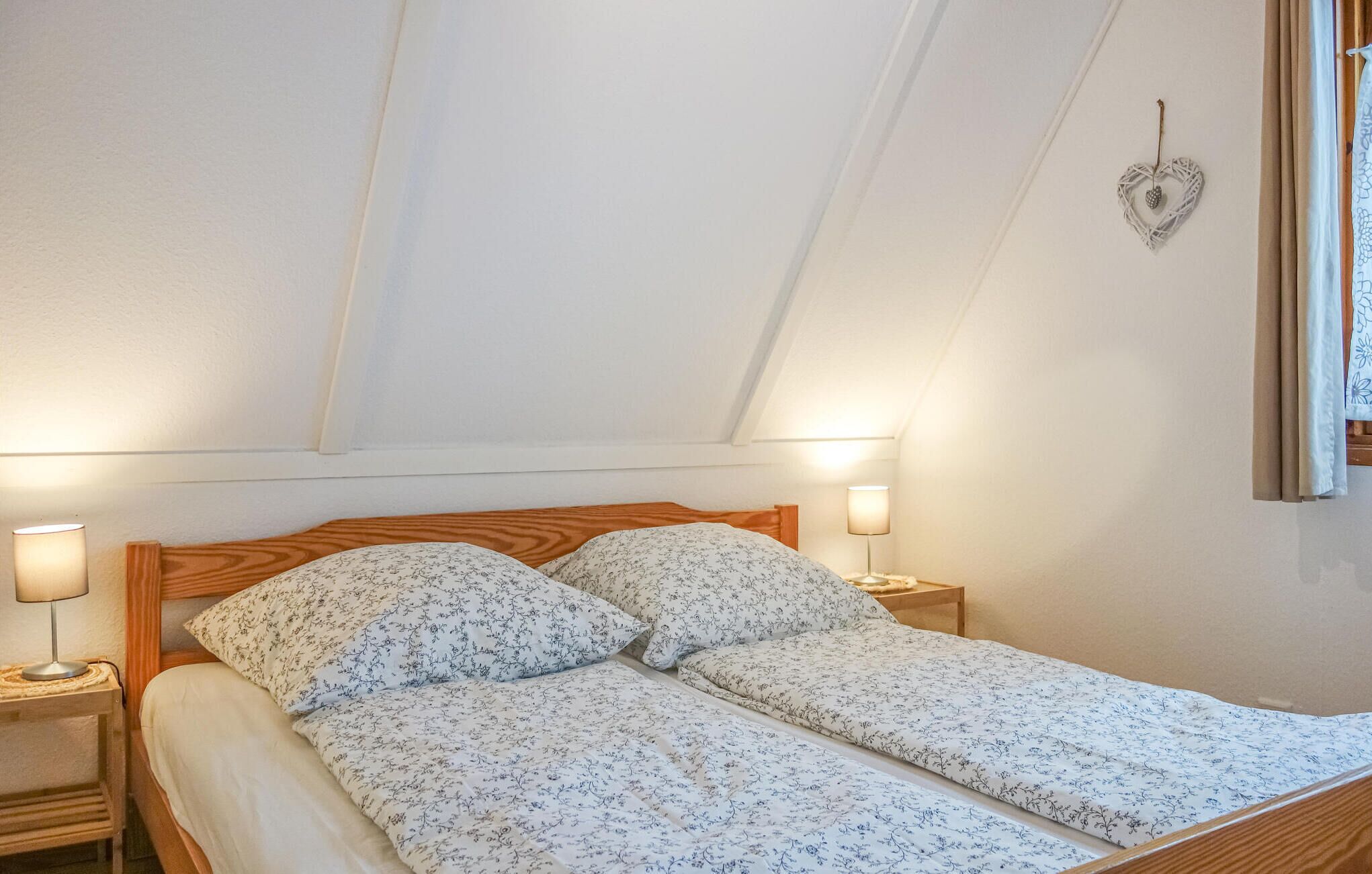Una camera da letto con testiera in legno, due comodini con lampade, una copriletto floreale e una decorazione a forma di cuore sul muro.