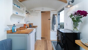 Cocina compacta con armarios de madera, un lavamanos y una estufa. Hay una silla y una mesa con un jarrón de flores.