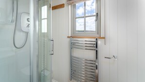 Un baño con cabina de ducha de vidrio, un perchero para toallas, una ventana con vistas y una puerta con picaporte de madera.