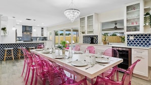 Una cuina moderna amb una illa central, armaris blancs i una zona de dinar amb cadires roses.