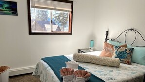 Una cama bien hecha con una colcha azul y blanca con motivos florales, una manta color turquesa y dos toallas dobladas al pie de la cama.