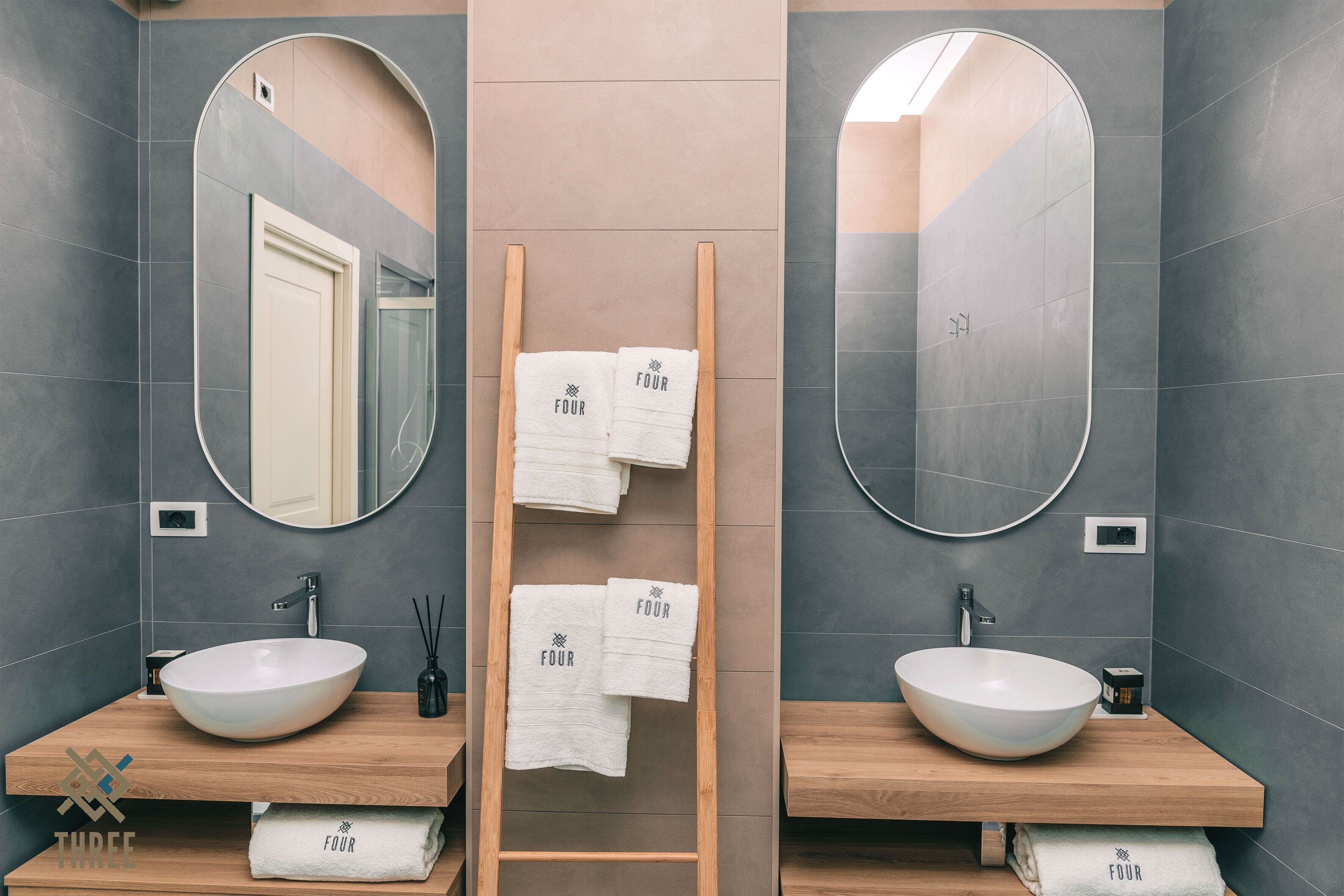 A modern bathroom with two sinks, large mirrors, and a wooden ladder with towels.
