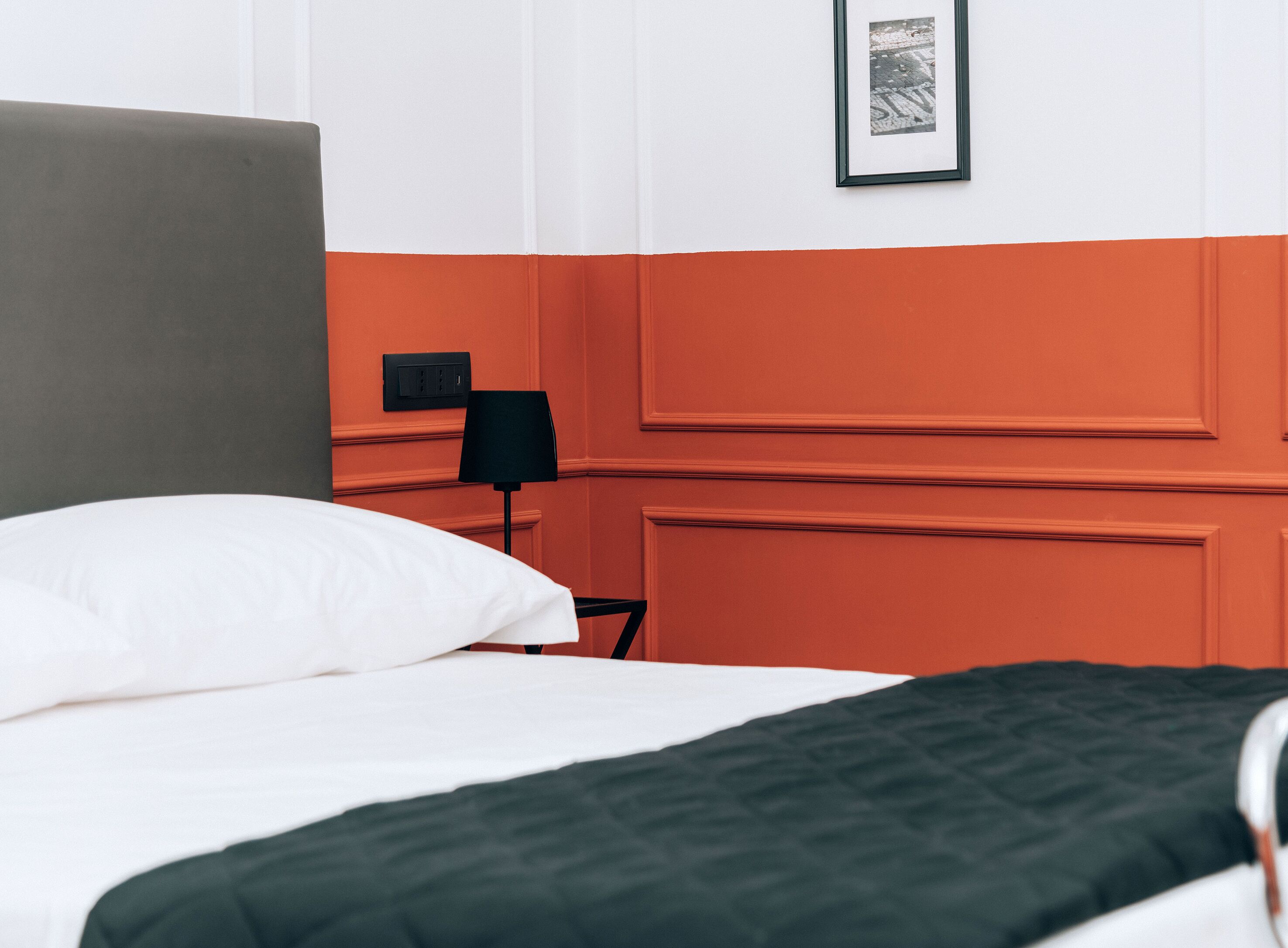 A bed with white and green bedding, a grey headboard, and a black lamp on a nightstand.