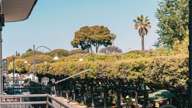 A balcony with a view of a street lined with trees and a café. - Four - Acanfora Suites (Pompei)