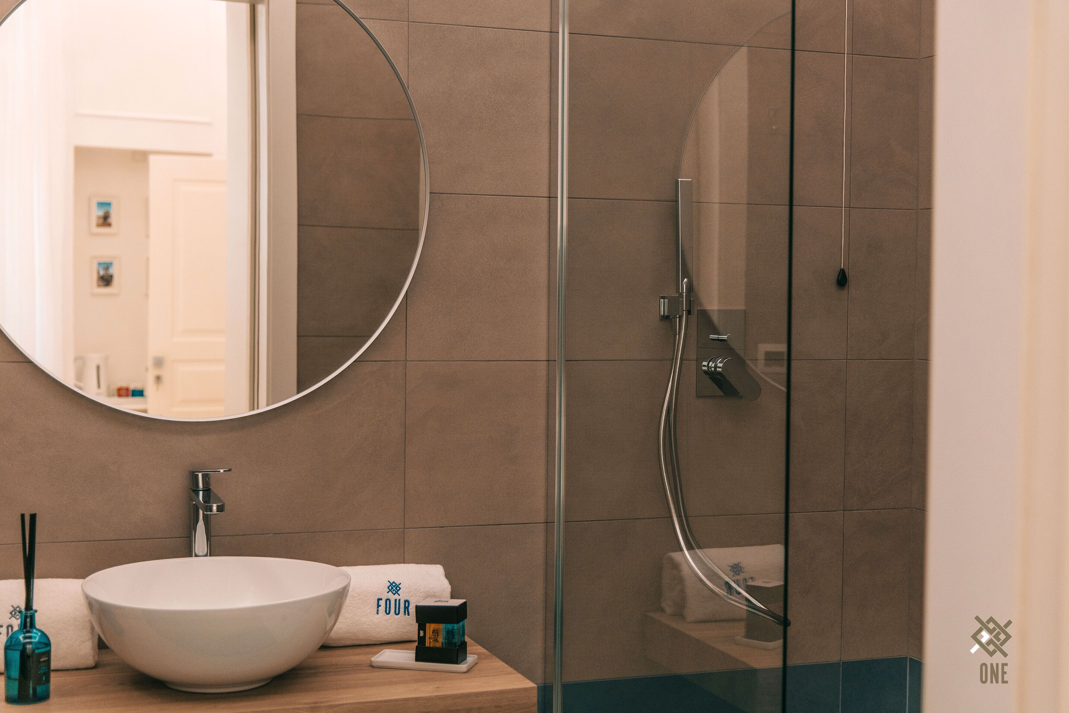 A bathroom with a round mirror, a white sink, and a glass shower enclosure.
