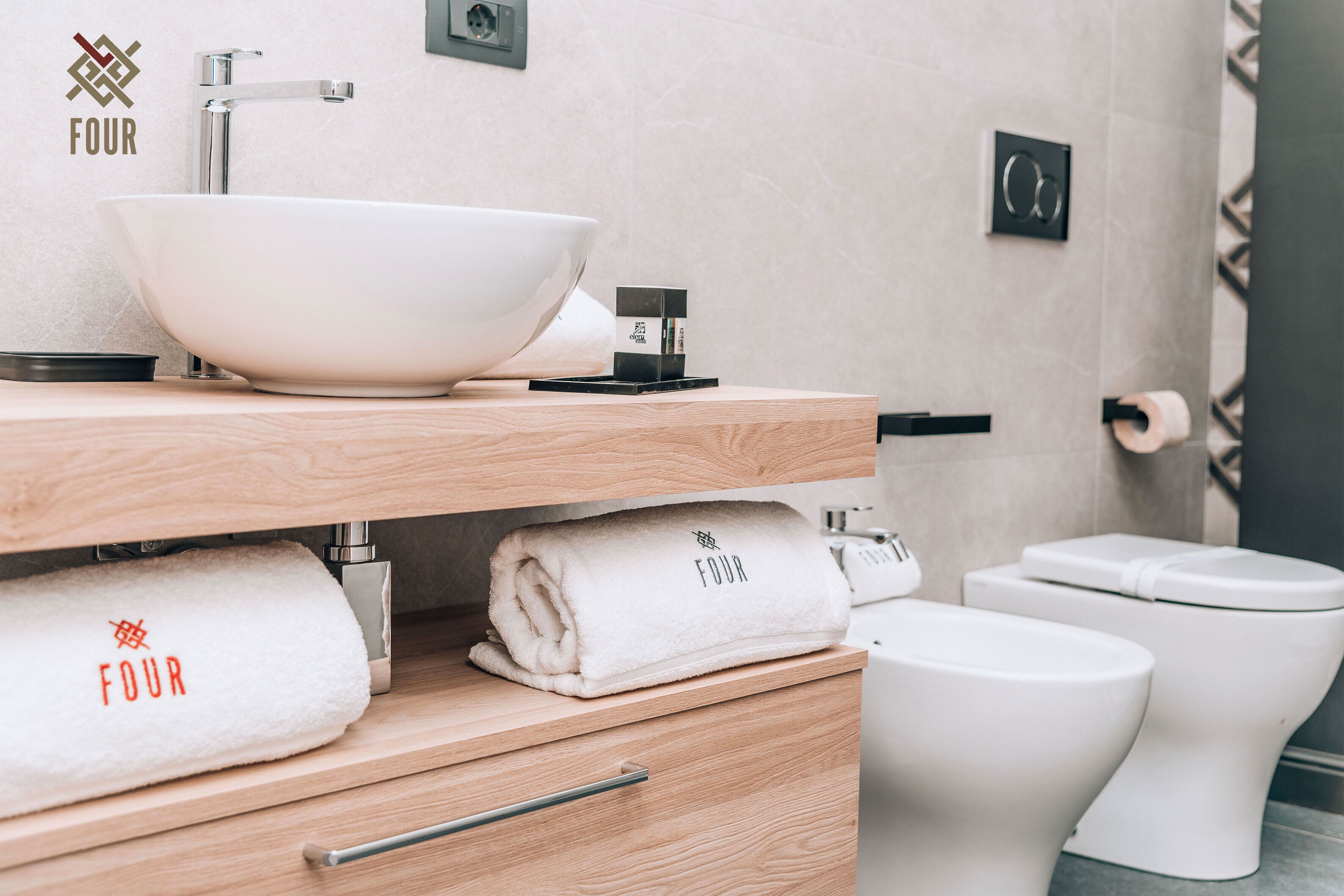 A modern bathroom with a white sink, two toilets, and a towel rack with towels.