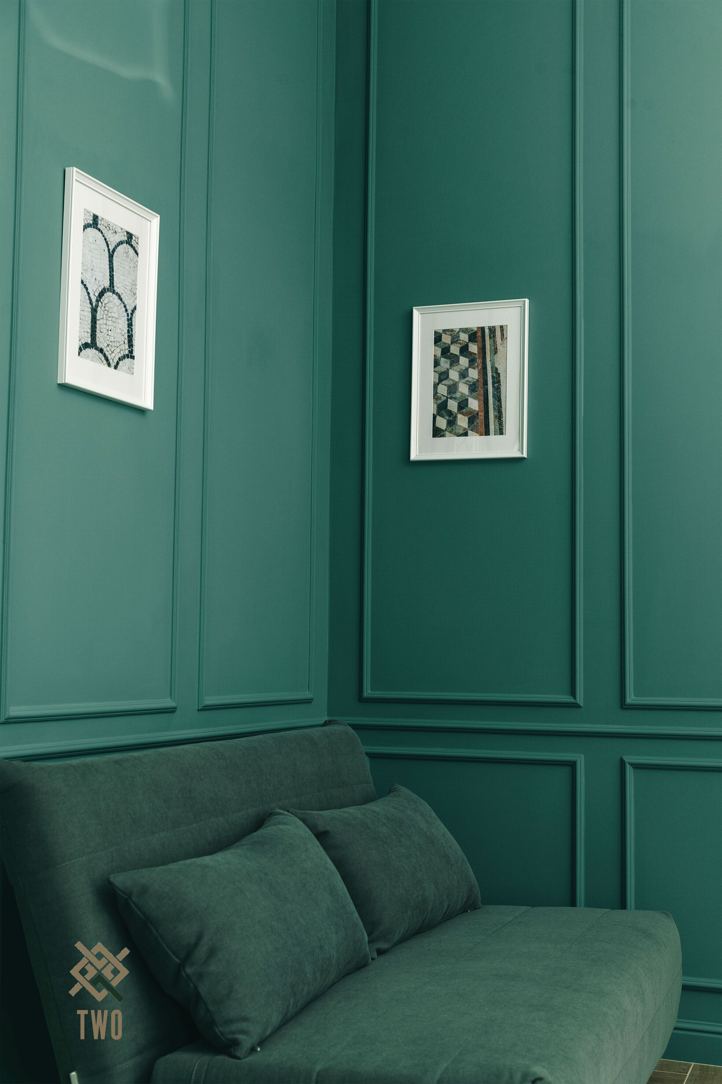 A teal-colored room with a sofa and two framed artworks on the wall.