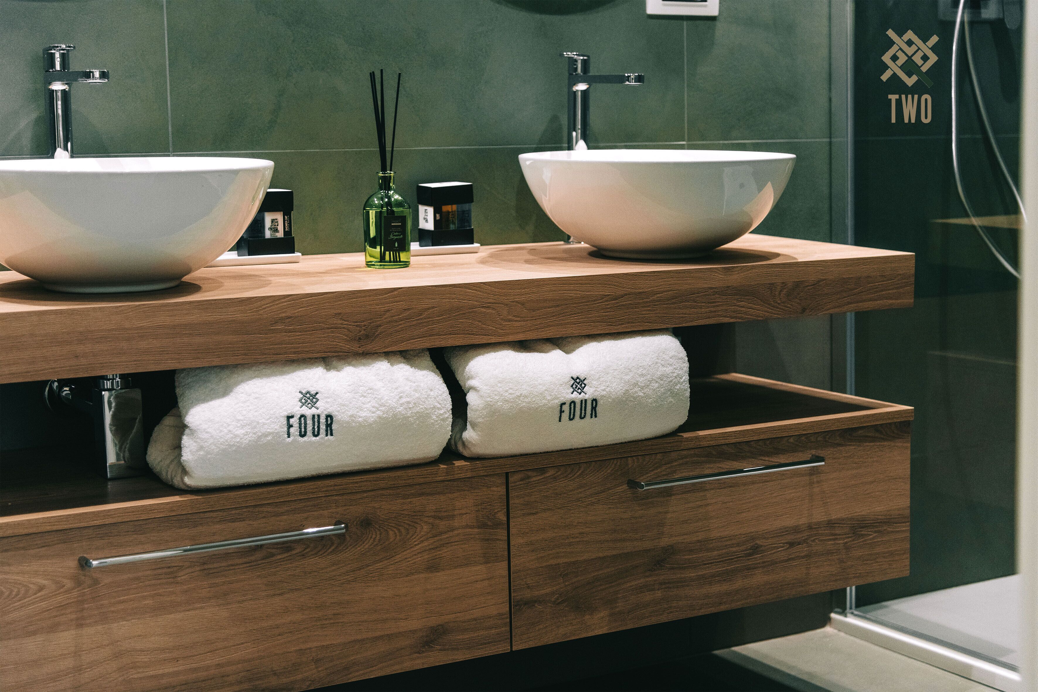 A bathroom with two large white sinks, wooden vanity, and two towels labeled "FOUR".