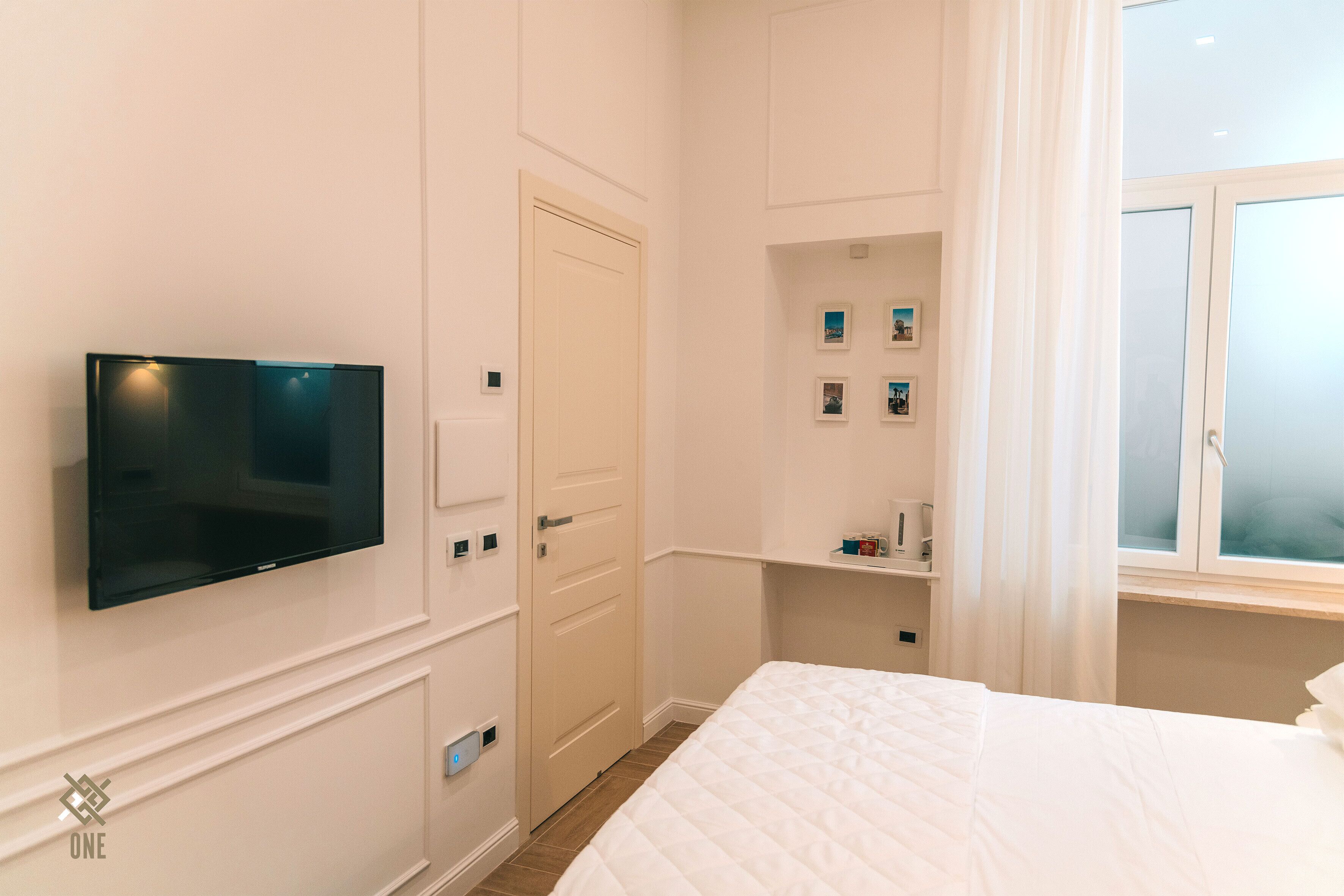 Una habitación de hotel con una cama, un televisor en la pared, una puerta y una ventana con cortinas.