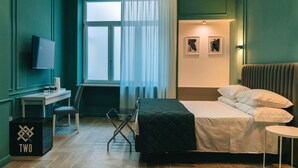 A hotel room with a bed, a desk with a television, a chair, a radiator, and a window with curtains. - Four - Acanfora Suites (Pompei)