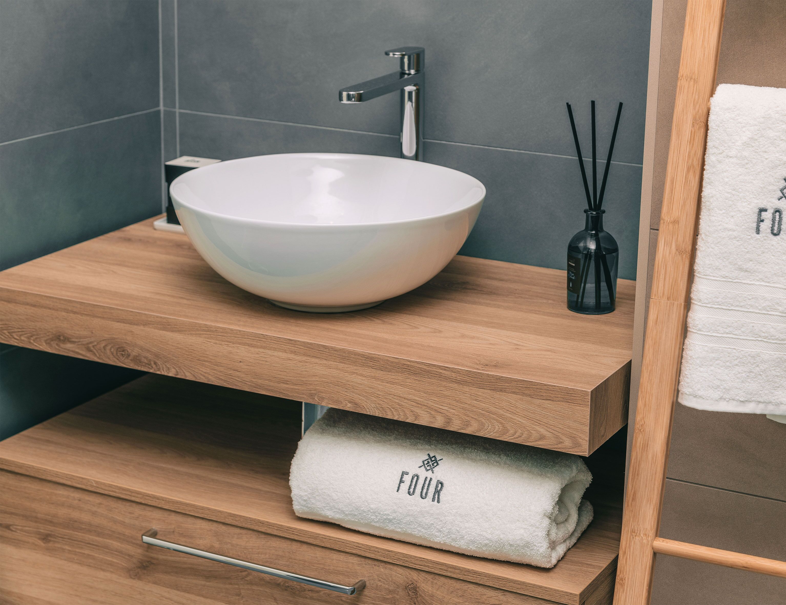 A bathroom with a white ceramic sink, wooden vanity, and a towel with "FOUR" on it.