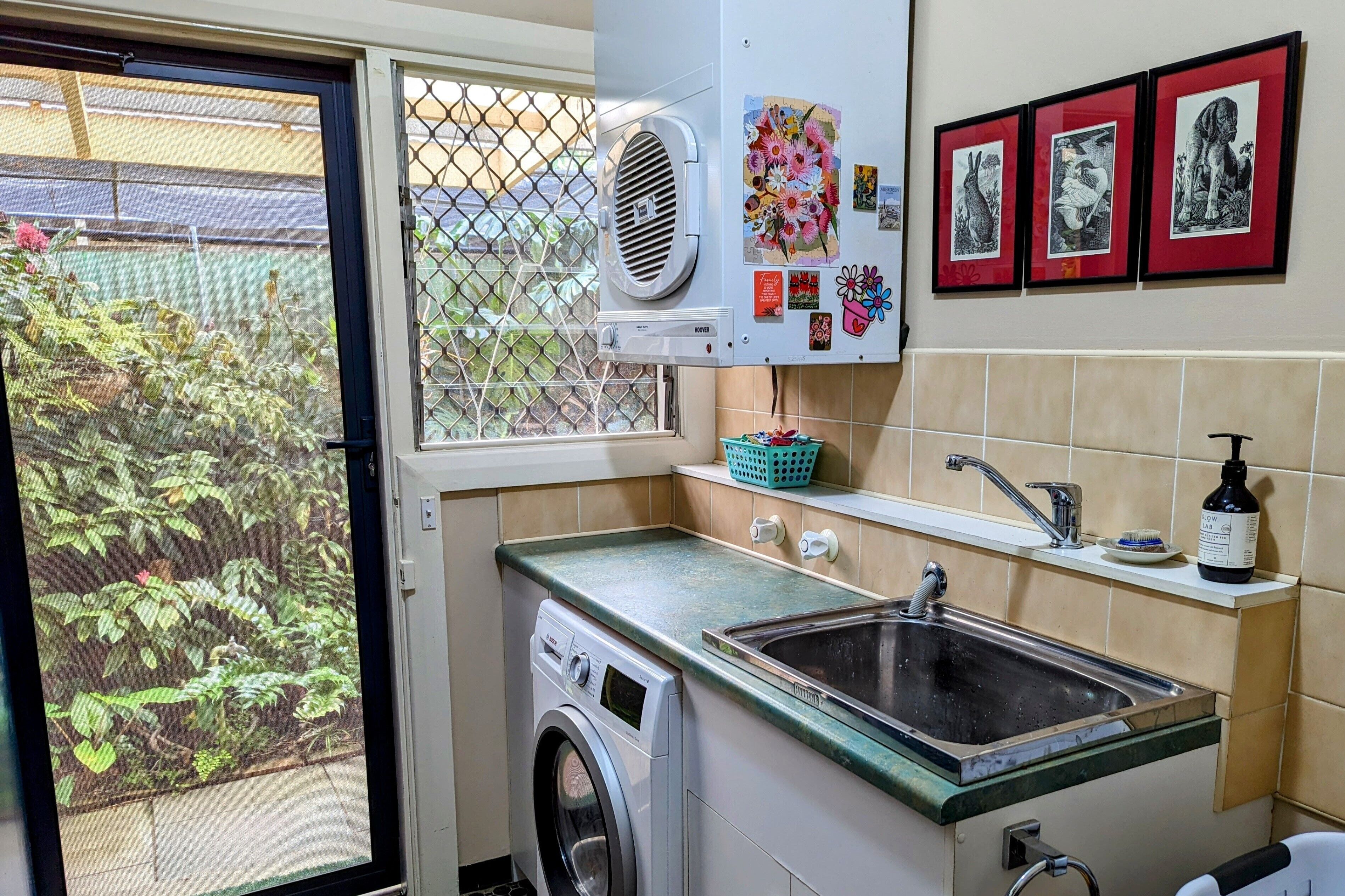 A compact kitchen with a washing machine, a sink, and a window with a view of greenery.