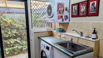 A compact kitchen with a washing machine, a sink, and a window with a view of greenery.