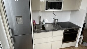 A compact kitchen with a stainless steel refrigerator, a microwave, a sink, and a dishwasher. - Chic and modern apartment (Châtillon)