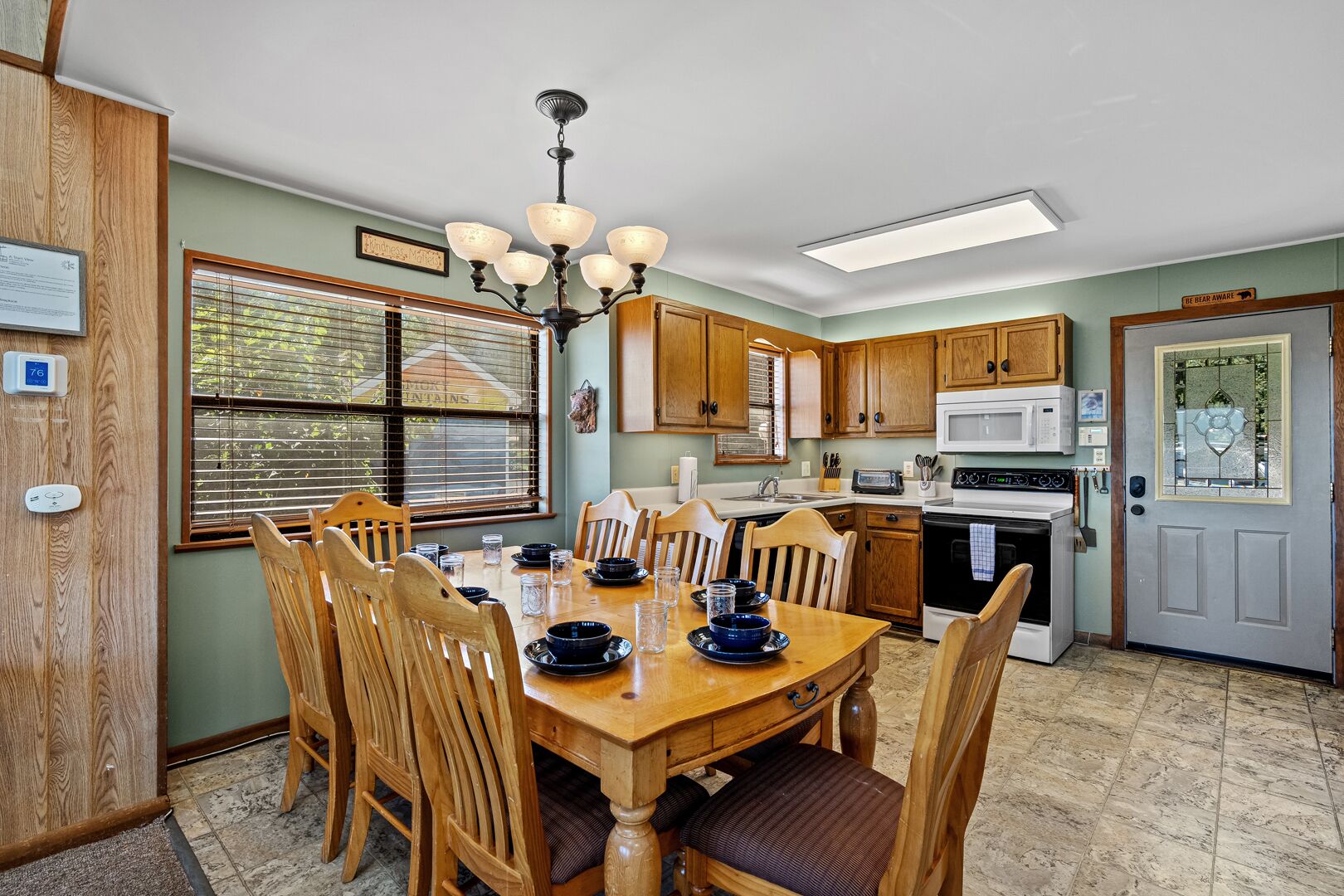 A dining area with a wooden table and chairs, a chandelier, and a kitchen with wooden cabinets and appliances.