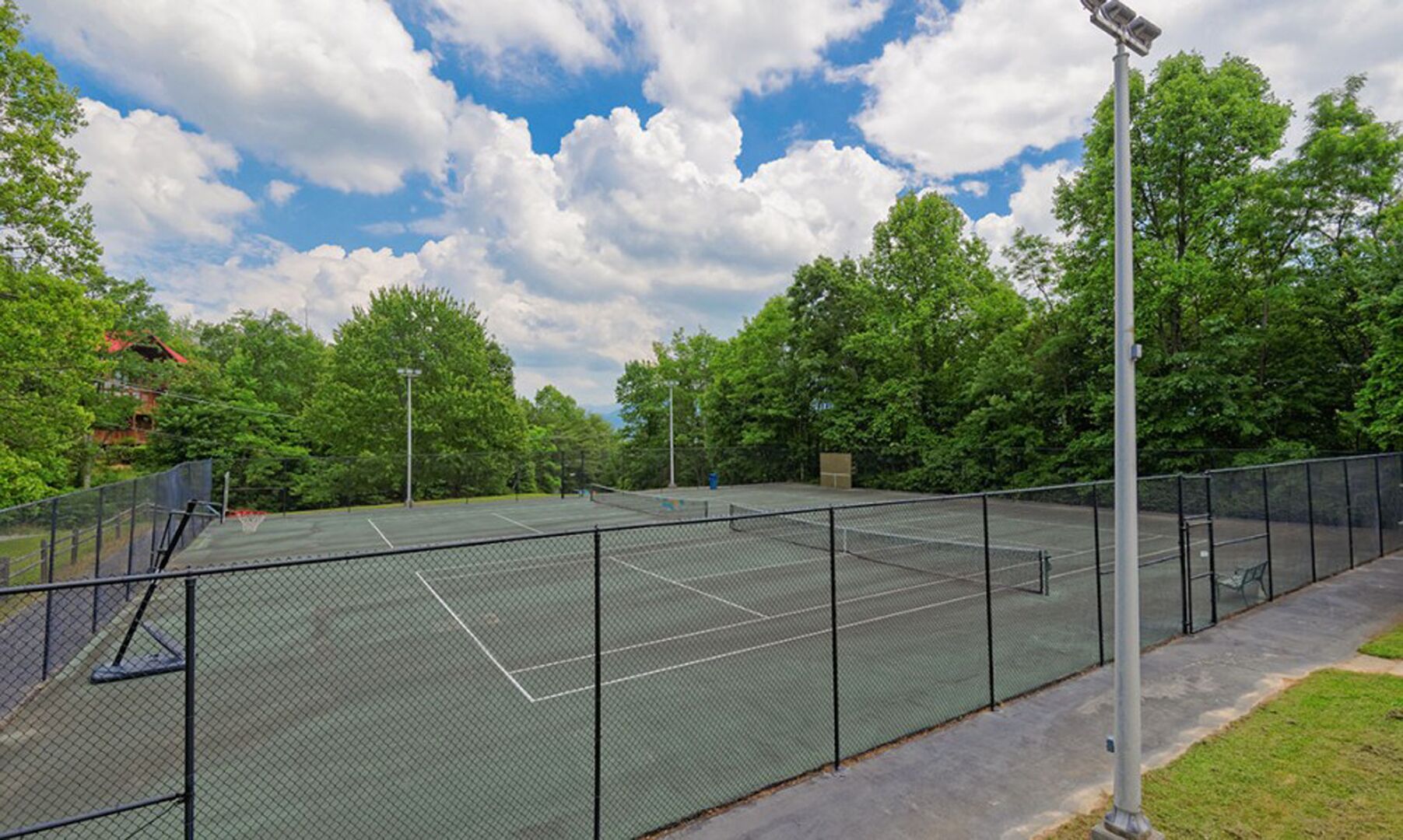 An outdoor tennis court surrounded by trees and a cloudy sky.