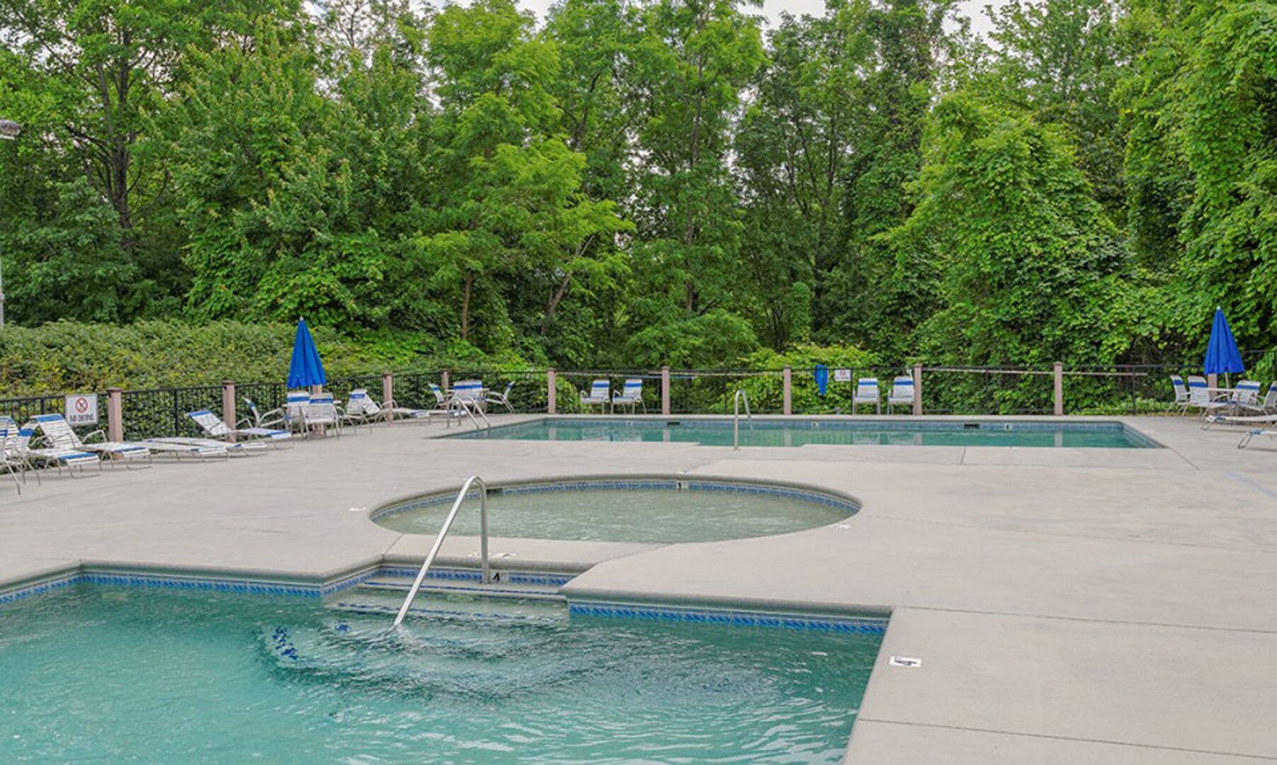 A swimming pool with lounge chairs and umbrellas, surrounded by trees.