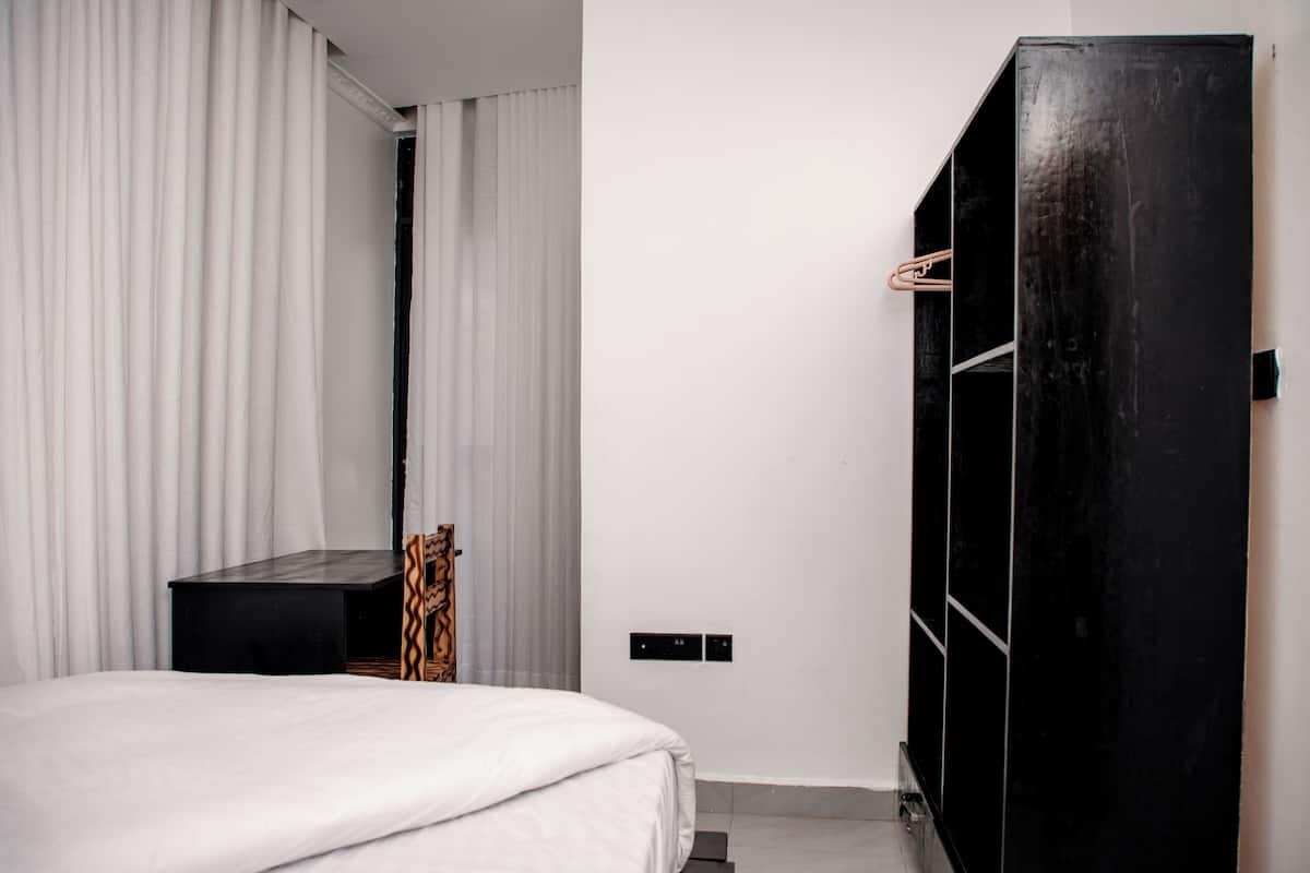 A modern bedroom with a bed, a black wardrobe, a small table, and a mirror.