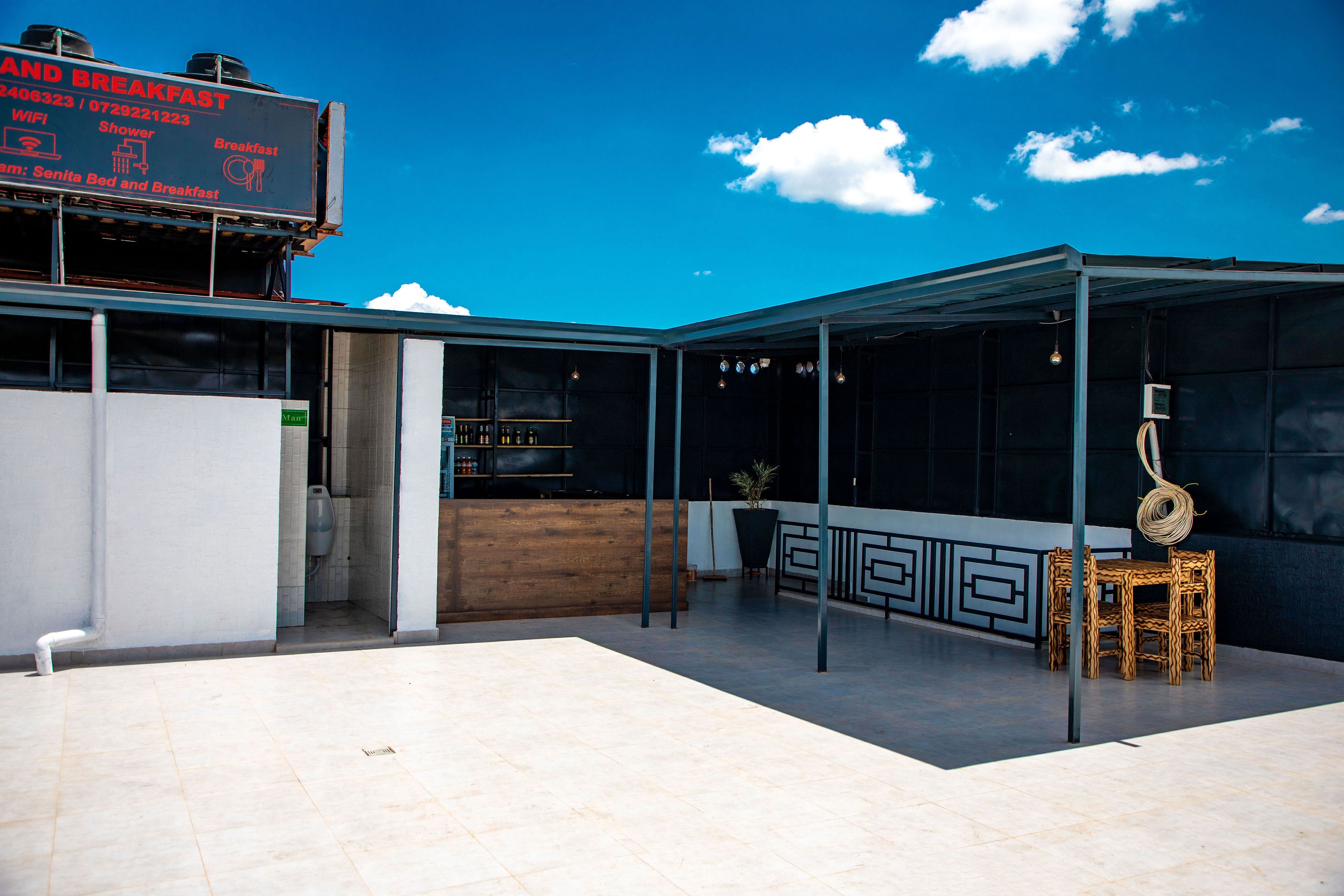 Et moderne udendørs opholdsområde med en overdækket terrasse, en bar og et skilt, der reklamerer for morgenmad.
