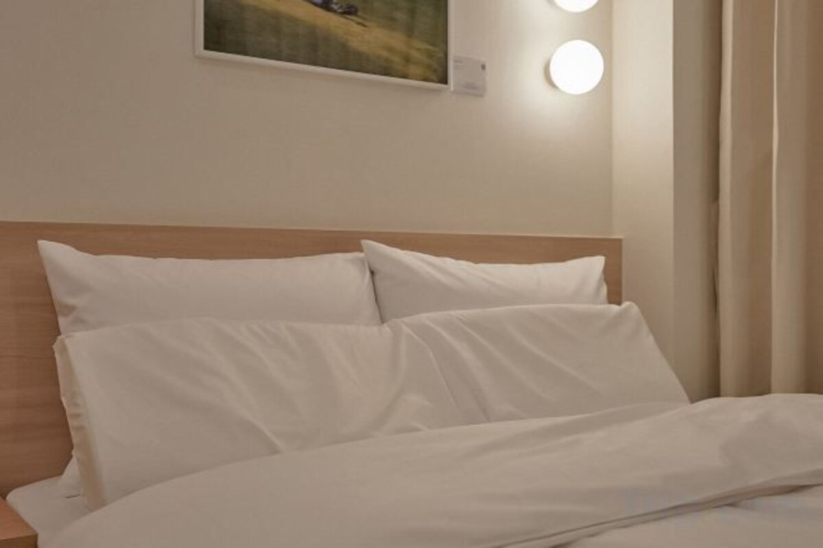 Un lit avec une literie blanche et une tête de lit en bois, dans une chambre d’hôtel.