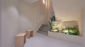 A modern staircase with a minimalist design, a small seating area with wooden stools, and a decorative plant arrangement with a sign.