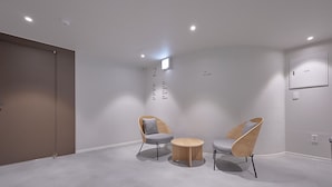 A modern, minimalist room with two chairs and a small table, a wall-mounted light, and a door.