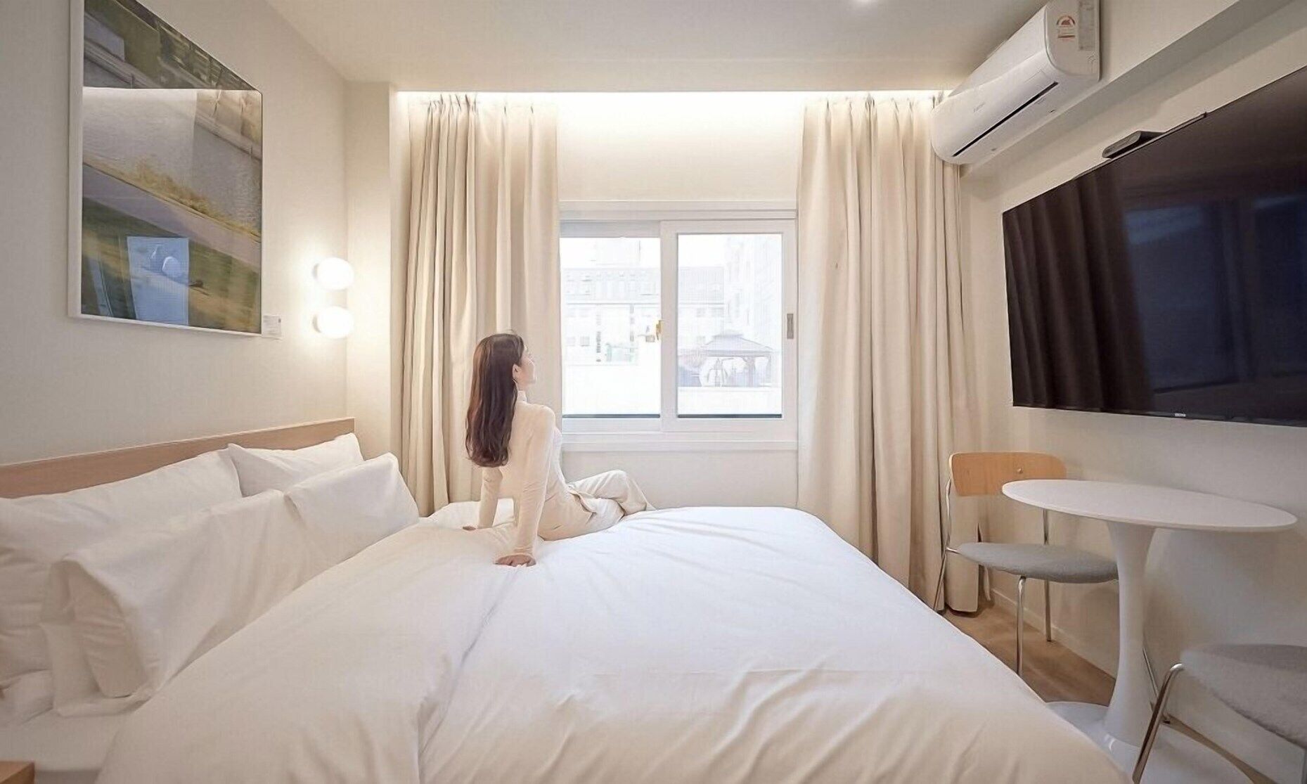 A hotel room with a bed, a TV, a small table, and a window with curtains.