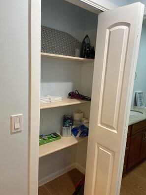 A partially open closet with shelves containing various items including a vacuum cleaner, a box of toilet paper, and cleaning supplies. - 3bedrm/2bath,near shopping center,freeway (Honolulu)